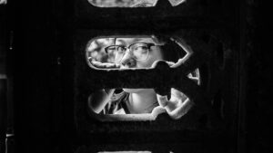 A young Asian woman peeking through a hole into the darkness beyond