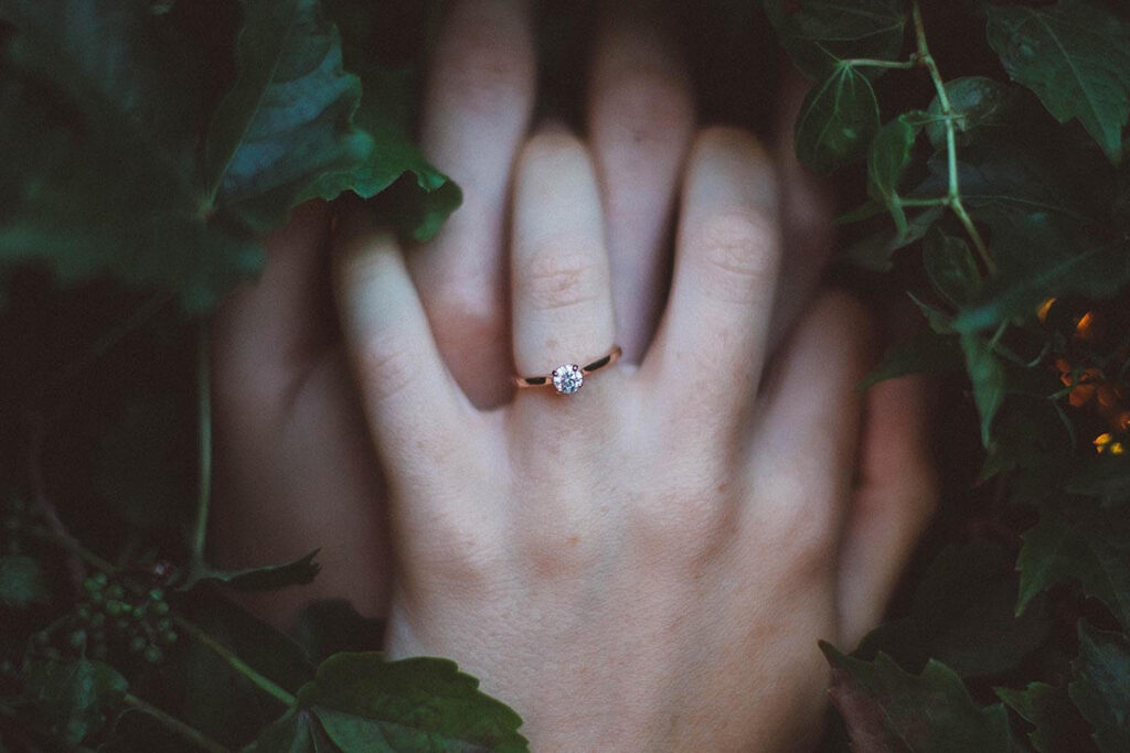 Two hands with wedding rings clasping each other in a bed of ivy.