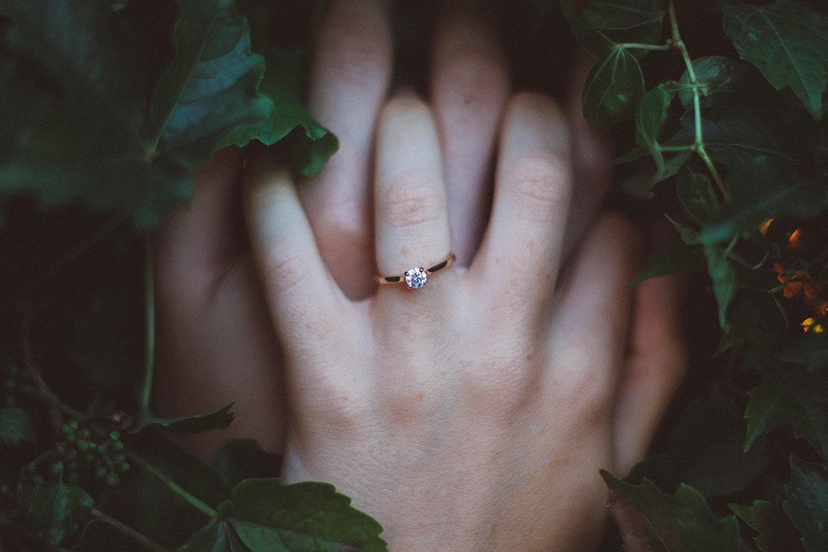 Two hands with wedding rings clasping each other in a bed of ivy.